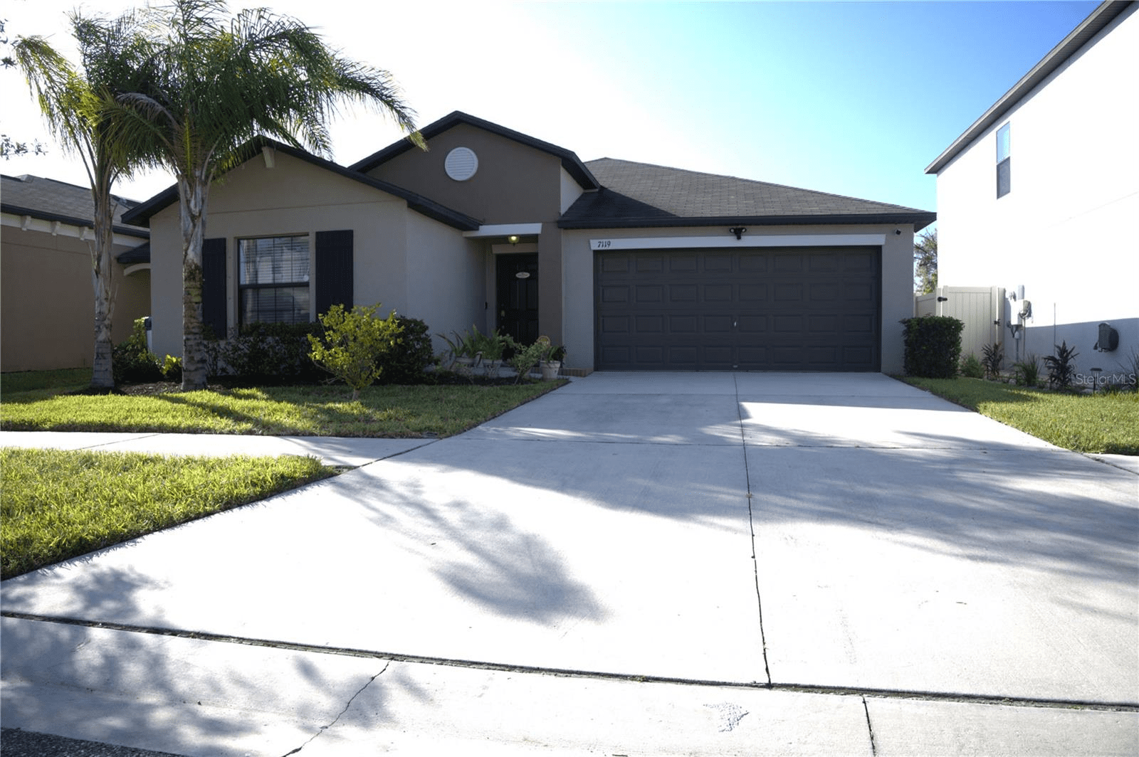 Suburban one-story house with a two-car garage and a palm tree in the front yard